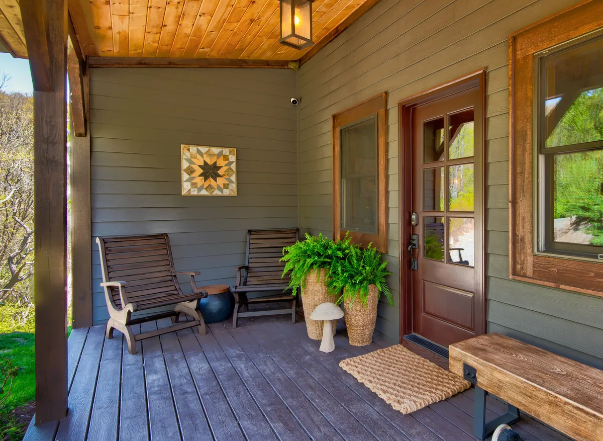 A close-up of the entrance area, showing wooden rocking chairs, potted plants, decorative wall art, and the front door. The image exudes a sense of comfort and peacefulness, suggesting a space where guests (and their pets) can settle in and enjoy the start of their stay.