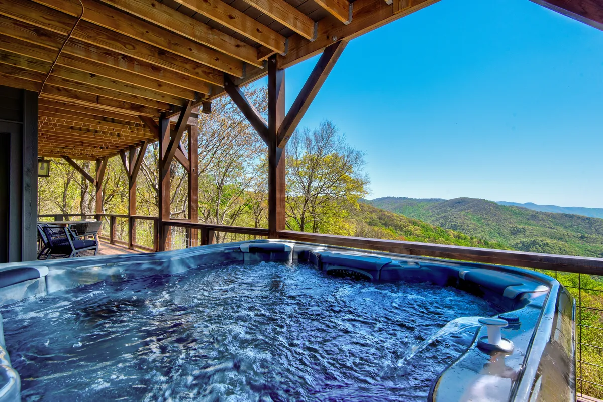A wooden structure frames a bubbling hot tub set against a backdrop of rolling hills and expansive mountain scenery. The area is peaceful and private, inviting relaxation after a day of adventure and exploration.