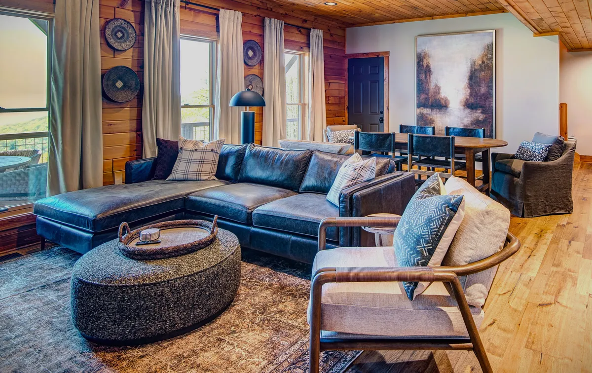 A large, comfortable sectional sofa anchors a welcoming living area, complemented by a round stone coffee table and artwork on the wall. The dining space in the background suggests easy transitions between activities, ideal for group gatherings, movie nights, or game nights.