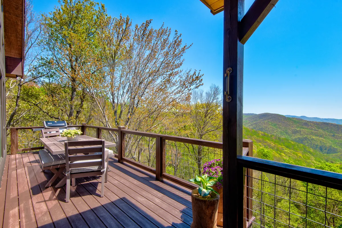 An exterior view of a stylish outdoor dining area featuring a table, grill, and potted plant, positioned on a deck with a sweeping mountain vista. The setting suggests al fresco dining with both sunset and morning views, seamlessly blending luxury living with the natural landscape.