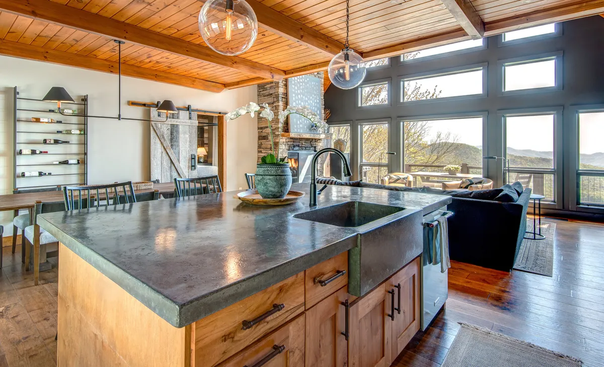 A gourmet kitchen with a central island, sleek stone fireplace, and expansive windows letting in natural light. There’s a dining area adjacent, making it ideal for family meals and entertaining. The design blends modern amenities with mountain charm.