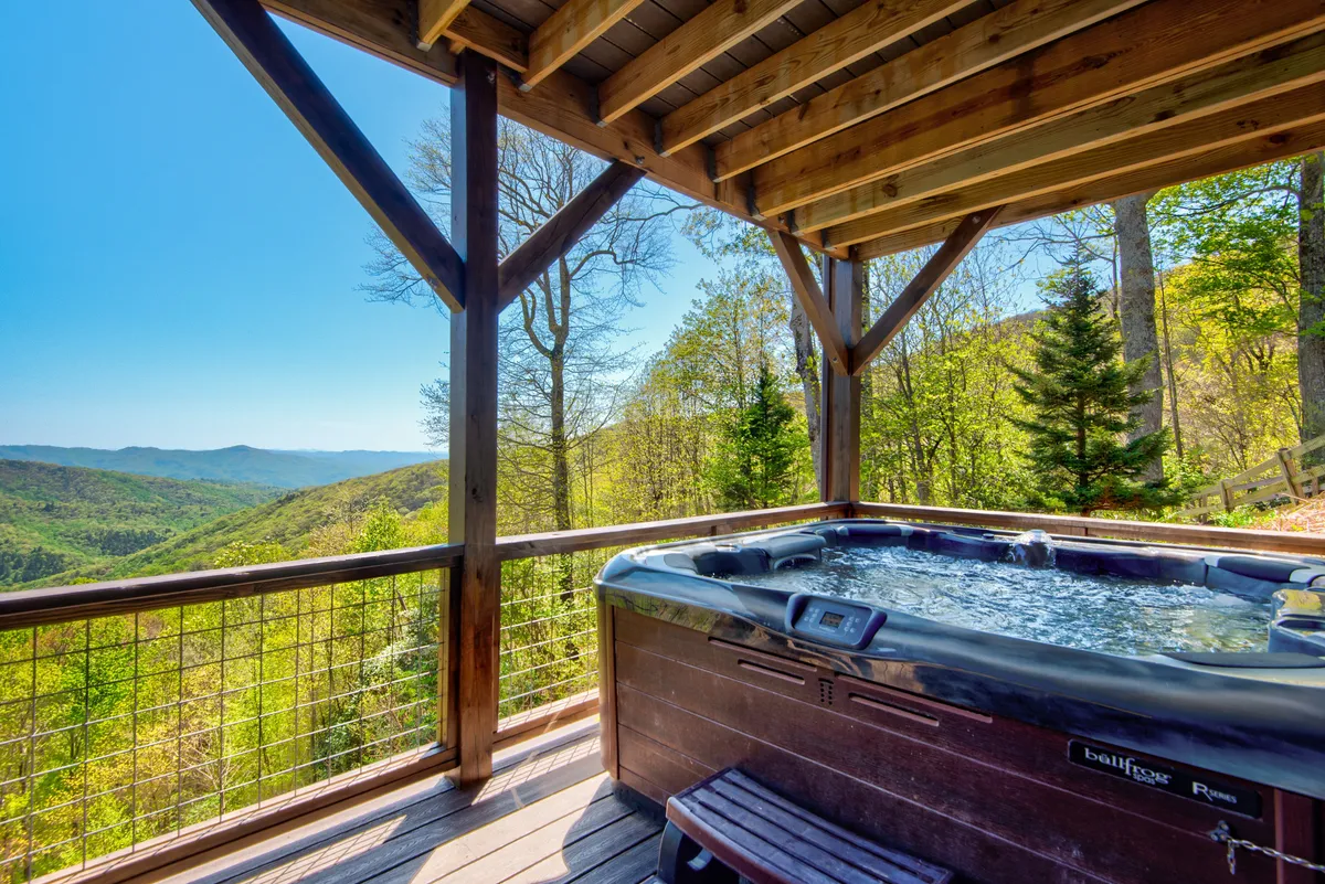 A tranquil outdoor hot tub set under a wooden structure, overlooking scenic mountain views. The setting is serene, designed for relaxation, and evokes the experience of unwinding beneath the stars or watching sunsets in comfort and privacy.