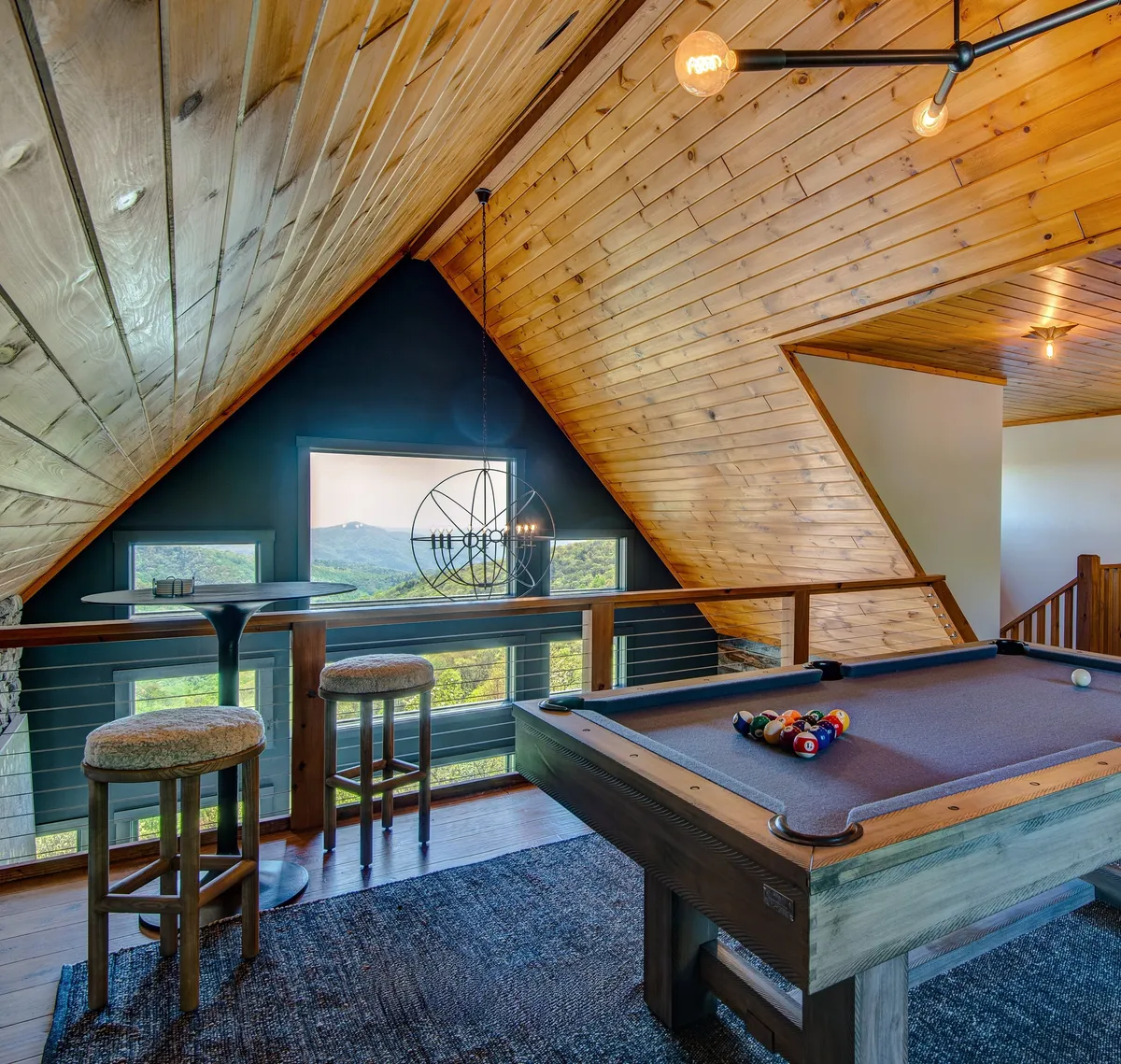 A recreational area with a pool table and bar stools set before impressive large windows, framing the picturesque landscape outside. The relaxed atmosphere and visible views evoke a sense of restful enjoyment after a day outdoors.