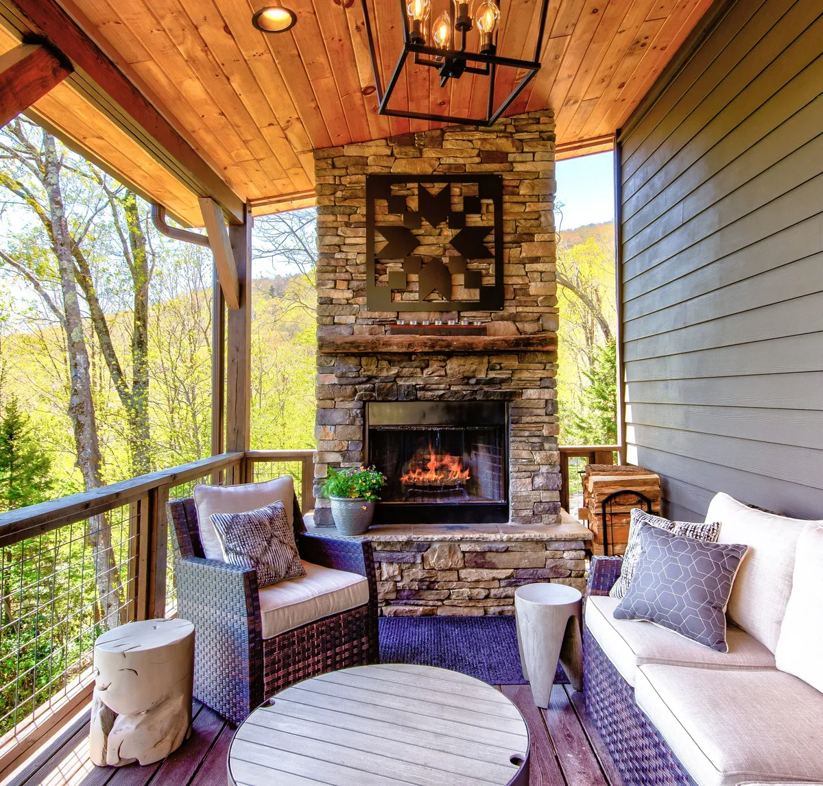 An outdoor living area on the main deck, centered around a dramatic stone wood-burning fireplace. Comfortable seating is arranged to enjoy both the warmth of the fire and the scenic surroundings, inviting guests to gather outside.